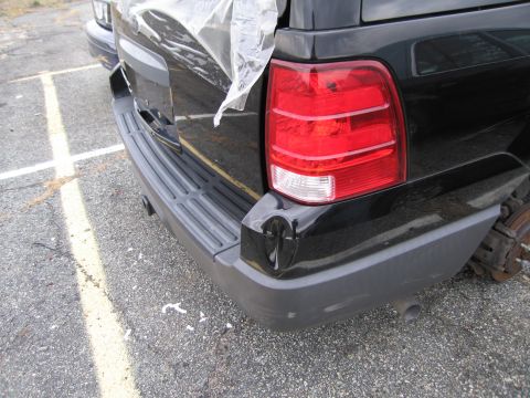 1991 Ford LTD Crown Victoria - Rear view of a black SUV showing a dented bumper and a missing wheel, with plastic covering the cargo area.