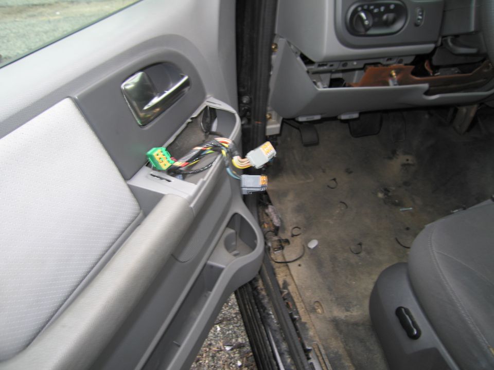 Car door panel with exposed wiring and connectors. Dashboard and floor visible