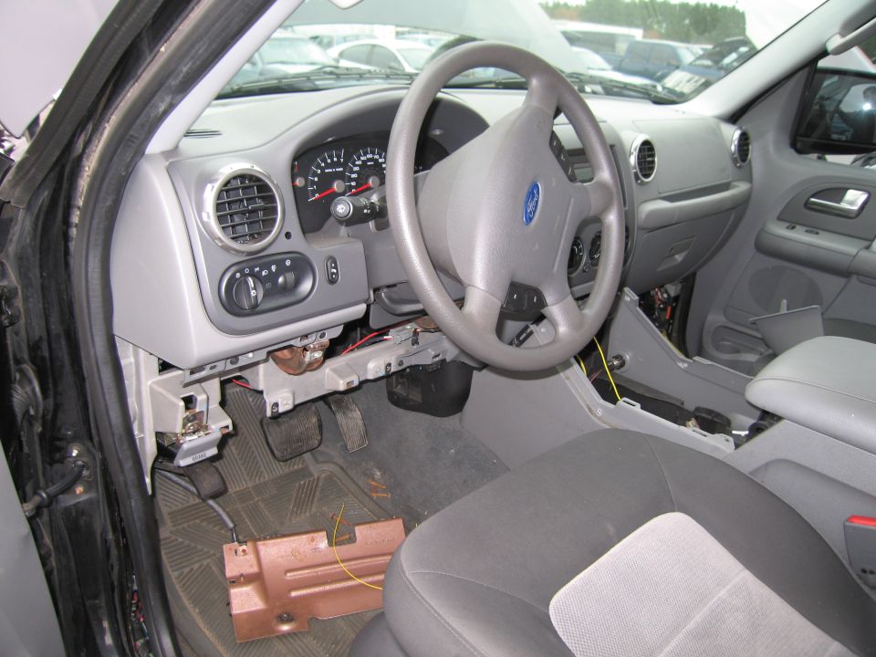 Car interior with dashboard, steering wheel, and seats visible. Some panels are removed