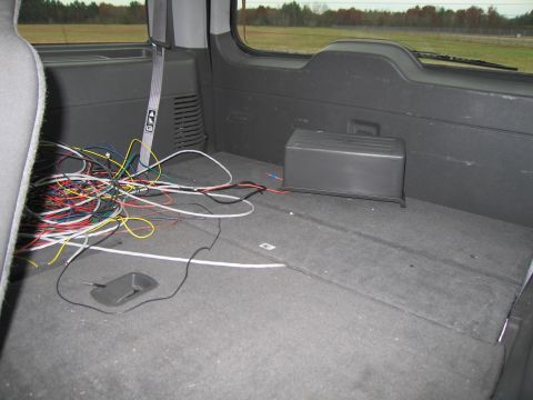 1991 Ford LTD Crown Victoria - The cargo area of a vehicle is filled with a tangled mess of electrical wires and a black storage box.