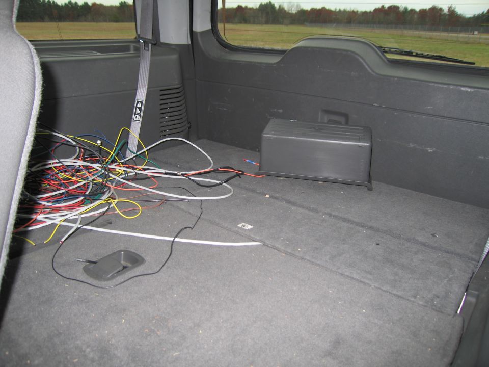 Interior cargo area of a vehicle showing a mess of colorful wires and a black box. A seat is visible on the left