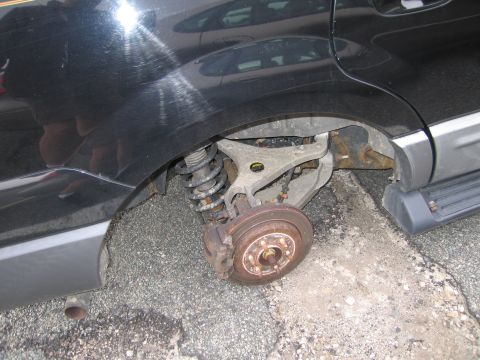 1991 Ford LTD Crown Victoria - The rear suspension of a dark SUV is visible, missing its wheel and showing a rusty brake rotor.