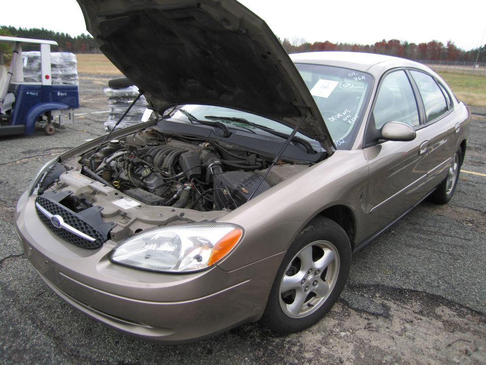 Tan Ford Taurus with hood open showing engine. Golf cart in background