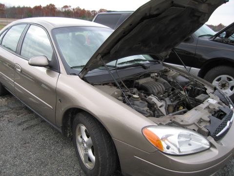 1991 Ford LTD Crown Victoria - A tan sedan with its hood open, revealing the engine compartment, parked next to a dark SUV.