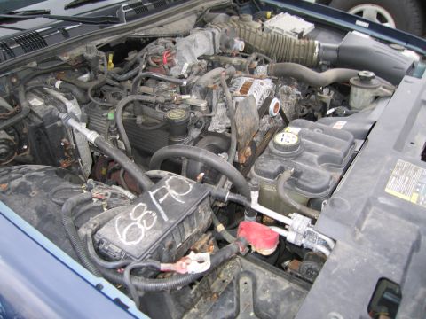 1991 Ford LTD Crown Victoria - The engine bay of a blue 1991 Ford Crown Victoria LTD is visible, with various components and a handwritten label on the fuse box.