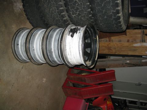 1995 Ford Ranger - A set of four tires are stacked, with four rims in front of them. The rims show signs of wear and tear.