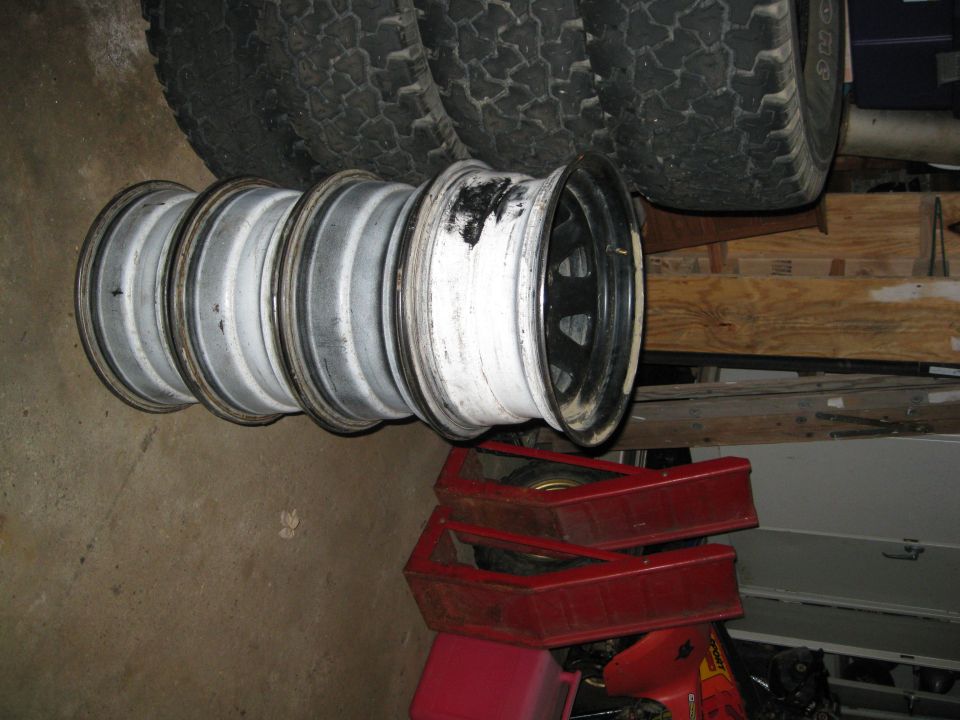 Four tires stacked with rims in front. Some rims are white, one is black