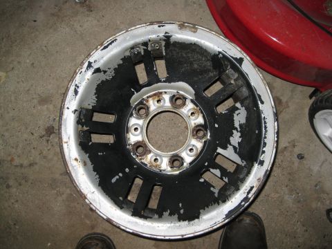 1995 Ford Ranger - This is a worn aluminum wheel with peeling black paint and rust around the lug holes.