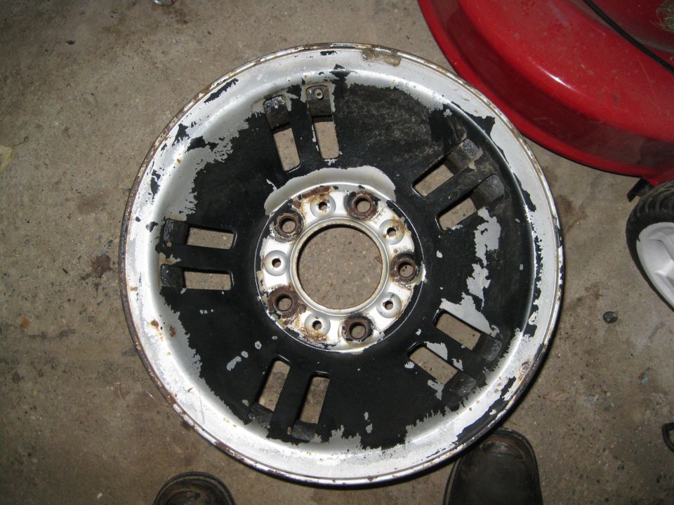 worn aluminum wheel with peeling black paint and rust around lug holes