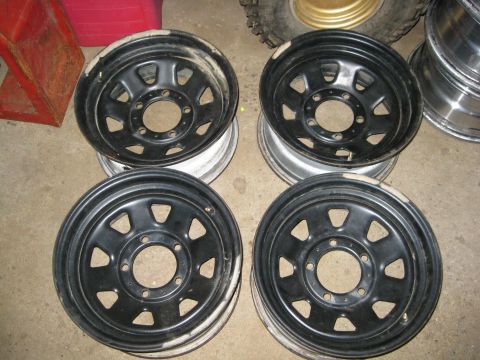 1995 Ford Ranger - Four black steel wheels are shown in a garage setting, with a red object and tires in the background.