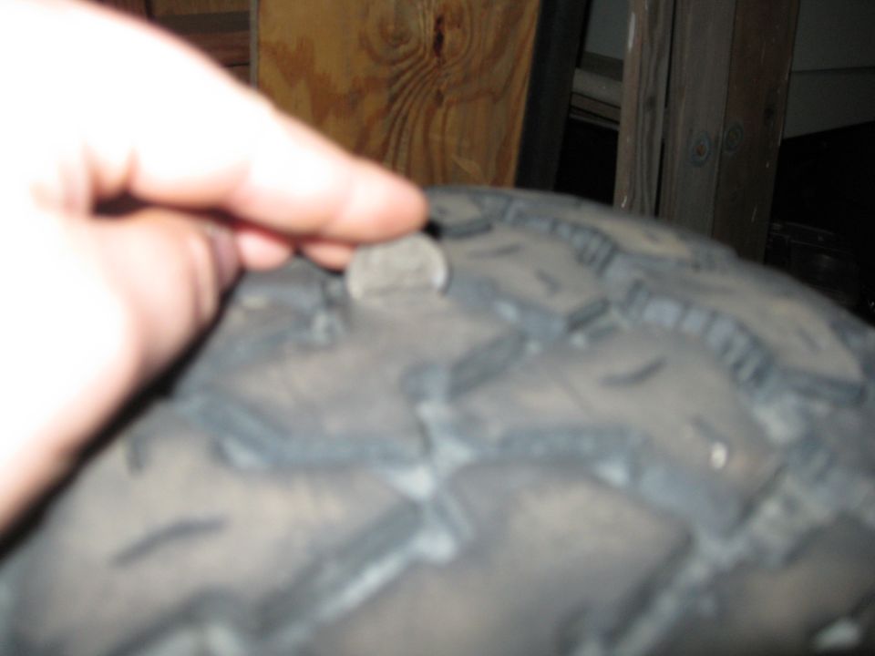 Finger pointing at a nail stuck in a tire tread