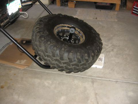 1995 Ford Bronco - A large spare tire is being weighed on a scale, with a tire carrier and part of a vehicle in the background.