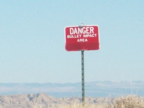 1985 Ford Bronco - A warning sign indicates a danger zone for bullet impacts in a remote, arid landscape.