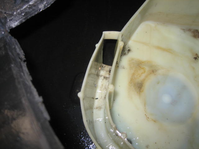 Close-up of a dirty white plastic fluid reservoir with a Supermotors.net watermark