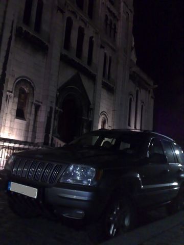 1991 Ford Crown Victoria - A dark colored Jeep Grand Cherokee is parked in front of a large, ornate building at night.