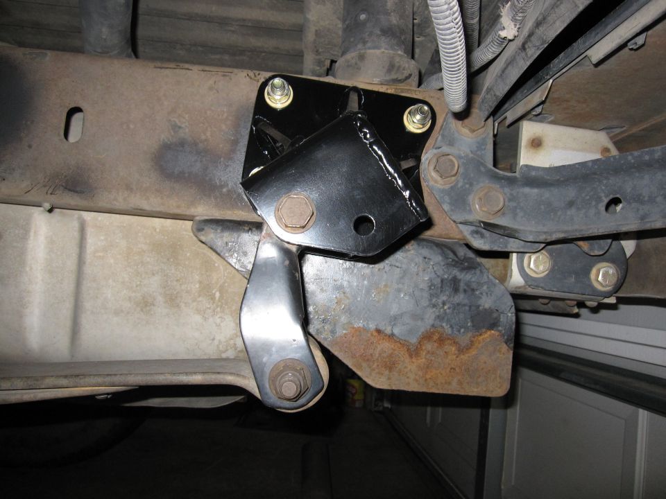 Black suspension bracket on frame rail with rusty factory components nearby