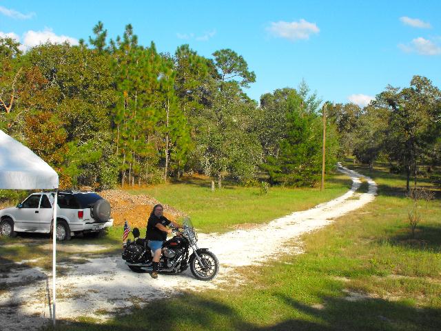 Black Harley cruiser with rider by a white SUV on a rural gravel drive