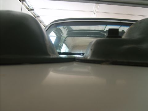 1989 Ford Bronco - The rear of a white Ford Bronco is visible between two dark gray fender flares, with windshield wipers on the glass.