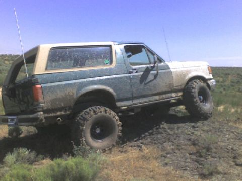 1989 Ford Bronco - This lifted Ford Bronco is covered in mud as it navigates a rough, outdoor landscape.
