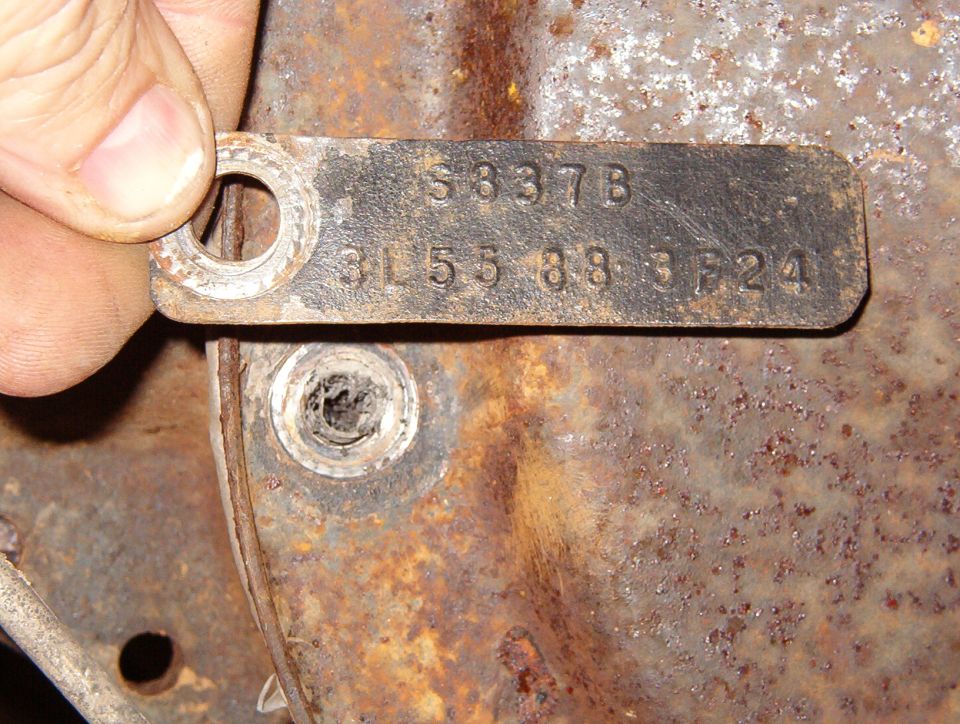 Metal axle identification tag stamped S837B held against a rusty housing