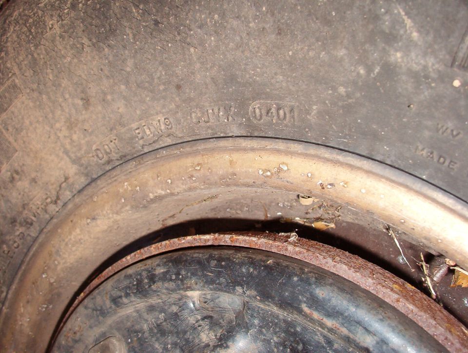 Close-up of tire sidewall DOT code 'EDW9 CJWX 0401' on a rusty steel wheel
