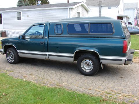 1984 Ford F-250 - This pickup truck features a two-tone paint job with a dark green body and silver lower trim, fitted with a camper shell.