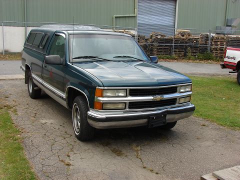1984 Ford F-250 - This pickup truck features a camper shell and a chrome grille, parked on a cracked asphalt surface.