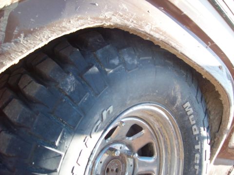 1985 Ford Bronco - Close-up of a tire and wheel well, showing mud and the 'Mud-Terrain' tire sidewall.