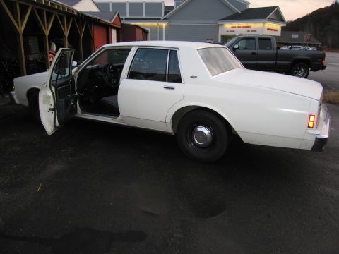 1991 Ford LTD Crown Victoria - A white four-door sedan is parked with its driver's side door ajar.