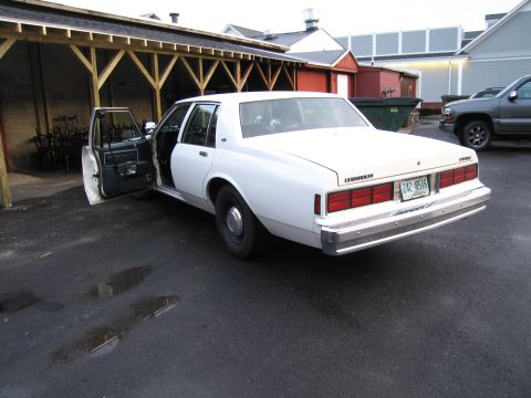 1991 Ford LTD Crown Victoria - This white sedan, likely from the 1980s, has its driver's door ajar, revealing a dark interior.