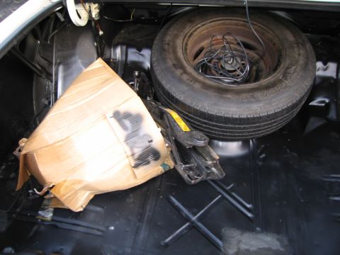 1991 Ford LTD Crown Victoria - The trunk of a car contains a spare tire, jack, and a large object covered in cardboard.