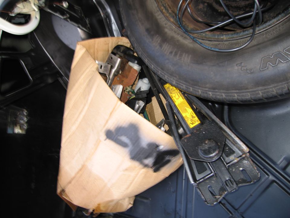 Car trunk interior with spare tire, jack, and a cardboard box of parts