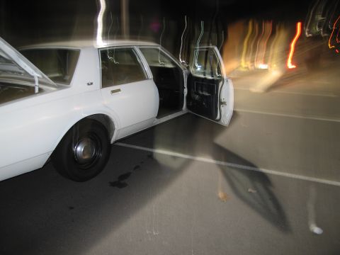 1991 Ford LTD Crown Victoria - A white sedan is parked with its trunk and driver's door open, illuminated by streetlights at night.