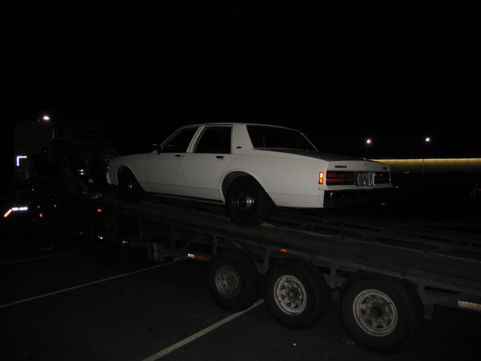White sedan on car carrier, rear view. Appears to be 1980s model