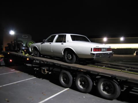 1991 Ford LTD Crown Victoria - Two cars are being transported on a car carrier trailer at night.
