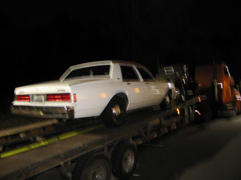 1991 Ford LTD Crown Victoria - A white sedan is loaded onto a flatbed truck for transport at night.