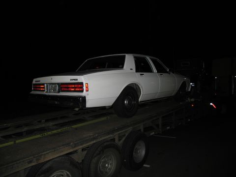 1991 Ford LTD Crown Victoria - A white sedan, identified as a Caprice, is loaded onto a flatbed trailer in the dark.