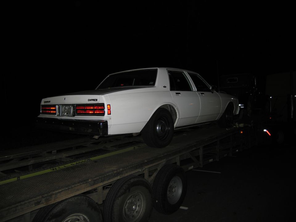 White sedan with 'Caprice' badge on rear, on a flatbed trailer at night