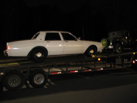 1991 Ford LTD Crown Victoria - Two vehicles are being transported on a car carrier at night.