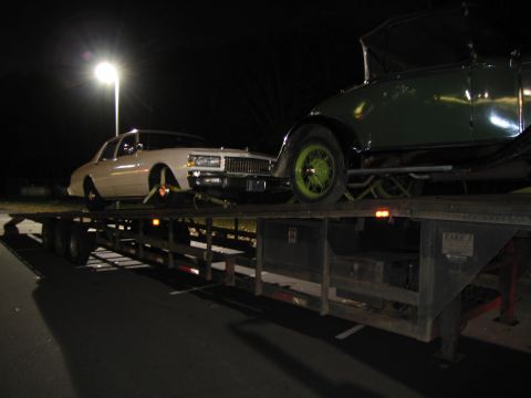 1991 Ford LTD Crown Victoria - A white sedan is transported on a flatbed trailer alongside a green vintage car under a streetlamp at night.