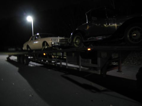 1991 Ford LTD Crown Victoria - A trailer carries two vehicles at night under a streetlamp.