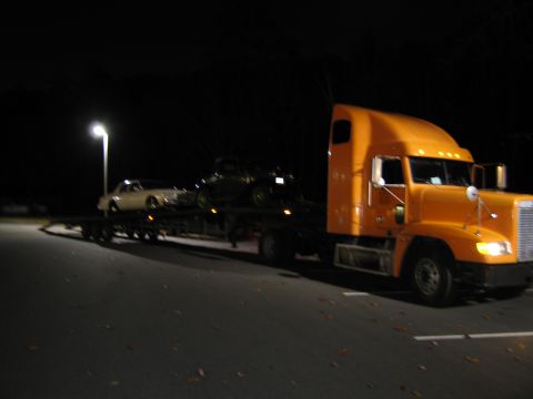 1991 Ford LTD Crown Victoria - A car carrier truck transports two vehicles at night under a streetlamp.
