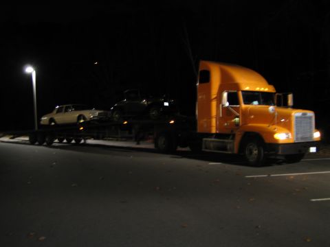 1991 Ford LTD Crown Victoria - A car carrier truck transports two vehicles at night under a streetlamp.