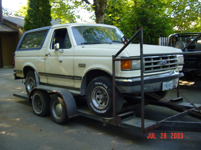 Tan Ford Bronco on a tandem flatbed trailer, front three-quarter, chrome grille, dated Jul 28 2003