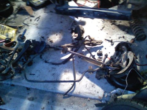 1969 Ford Mustang - Various disassembled vehicle suspension components are laid out on a concrete floor, suggesting a repair or build process.