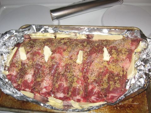 1978 Ford Bronco - Raw ribs are prepared for cooking with butter and seasonings in a foil-lined baking pan on a stovetop.