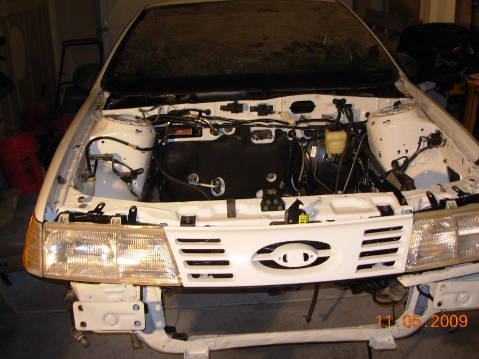 White sedan front partially disassembled, exposed engine bay, in a garage