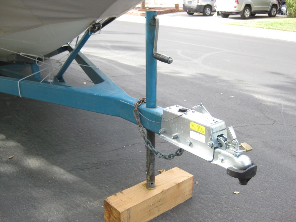Boat trailer tongue with blue frame, silver coupler, jack, and safety chains on a wooden block