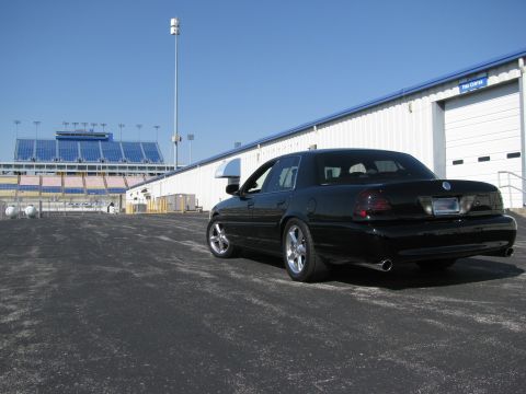 2003 Mercury Marauder - A black 2003 Mercury Marauder is parked near a racetrack grandstand and building.