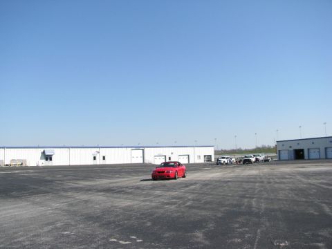 2003 Mercury Marauder - A red convertible is parked in a large asphalt lot with several other vehicles and industrial buildings under a clear blue sky.
